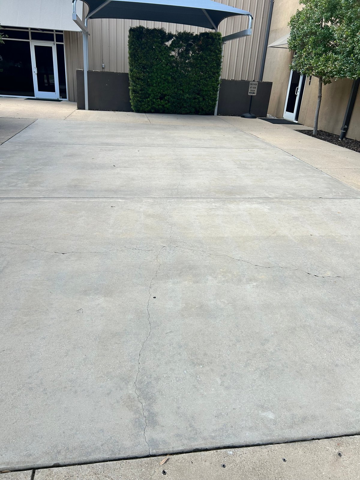 Empty concrete parking lot or patio with metal warehouse building and green ivy-covered wall in background